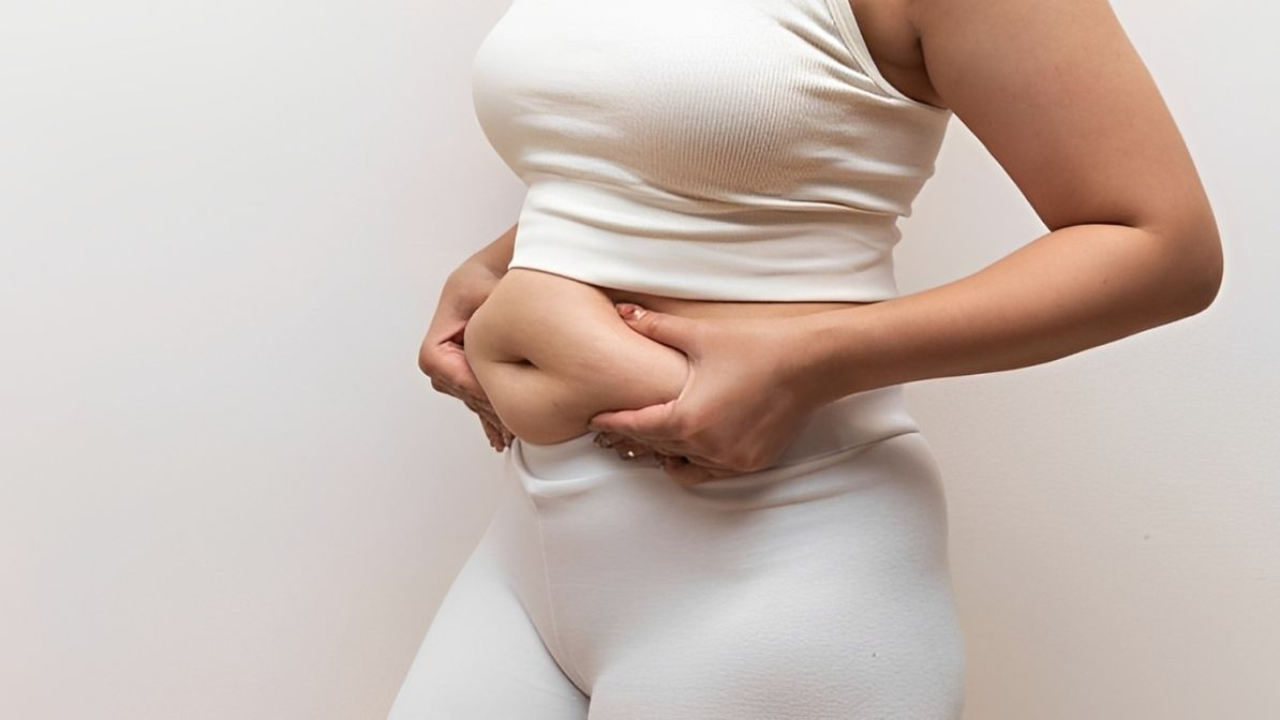 Woman holding belly fat, highlighting the importance of strength training and nutrition for women over 40.