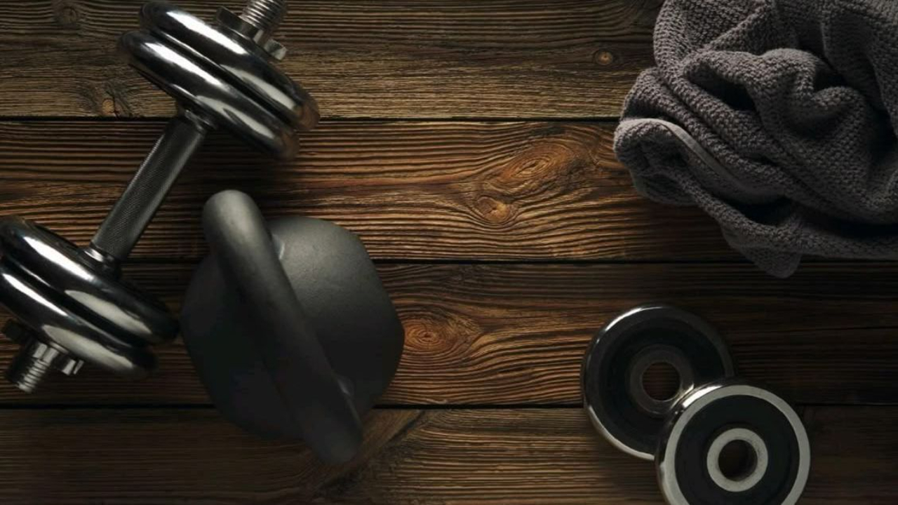 Dumbbells, kettlebell, and workout towel arranged on a dark wooden floor, representing strength training and fitness for women over 50 focused on building energy, vitality, and healthy aging.