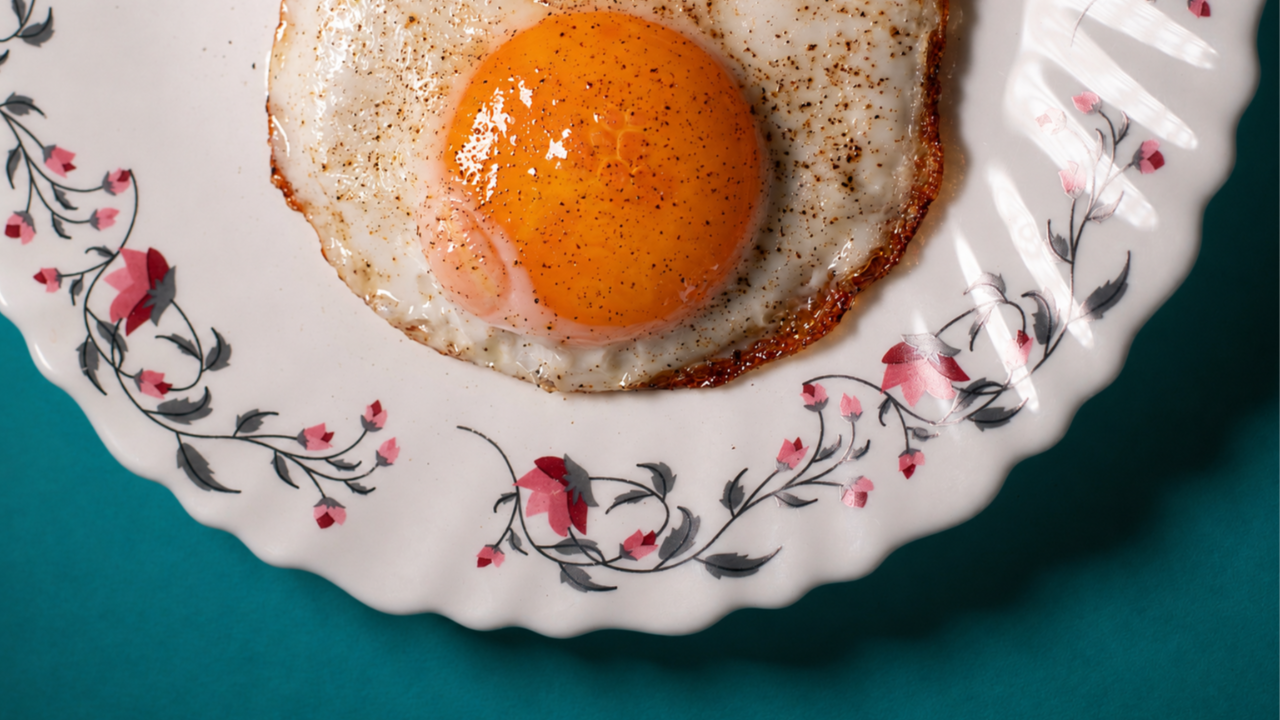Close-up of a sunny-side-up egg on a decorative plate, highlighting a protein-rich breakfast that supports women's energy, muscle health, and lean body composition.