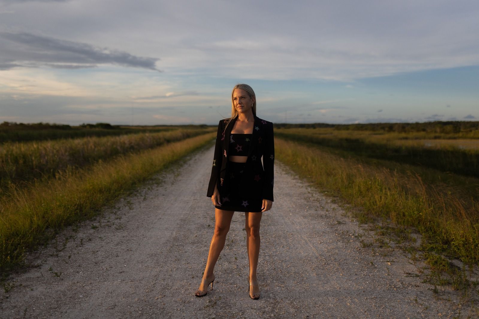 Shelly standing on an open road at golden hour in a black star-embroidered suit