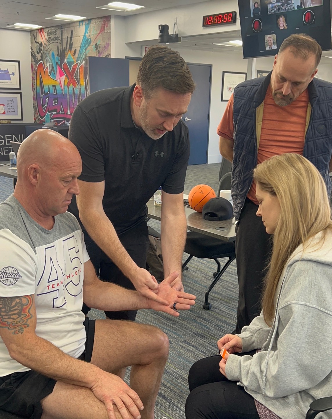 Matt Bush stands with three Next Level Neuro students in a classroom setting. One student's hand is outstretch while Matt is showing the group how to perform an applied neurology assessment