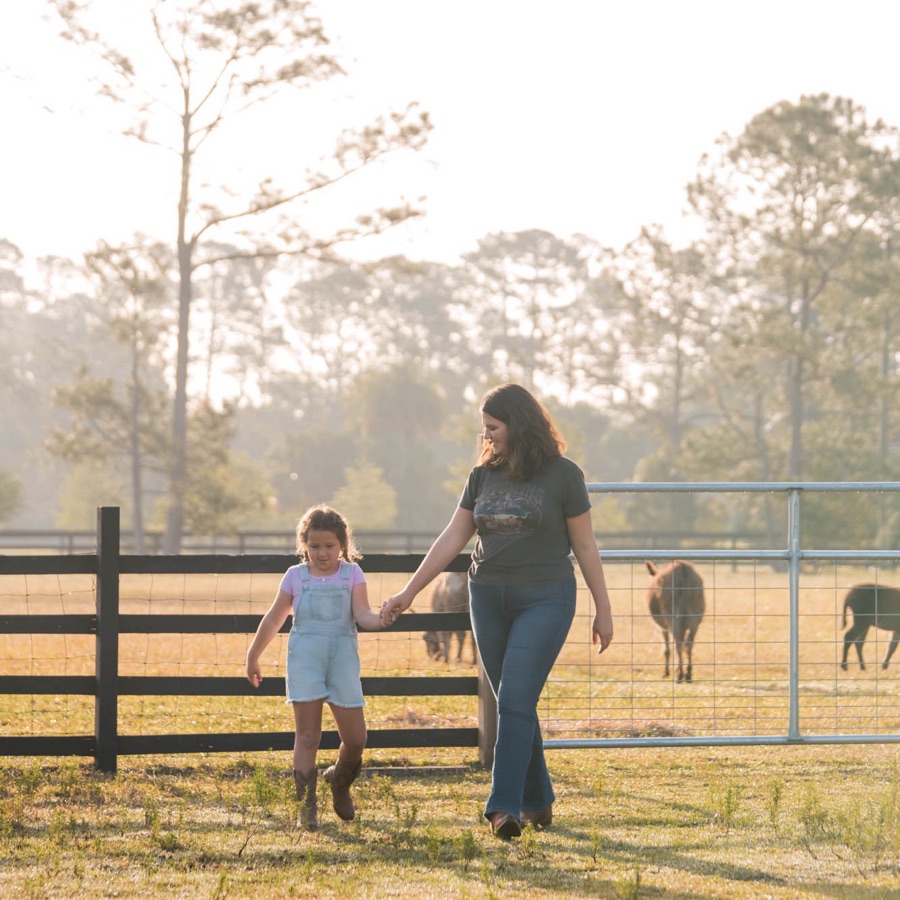 Taylor walking hand in hand with her daughter past the horse pasture