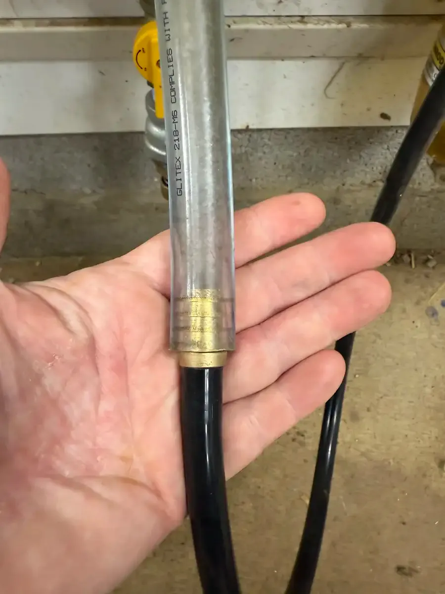 Hand holding a brass reducer and silicone hose attached to the cut vacuum line for Dexter cow milking setup.