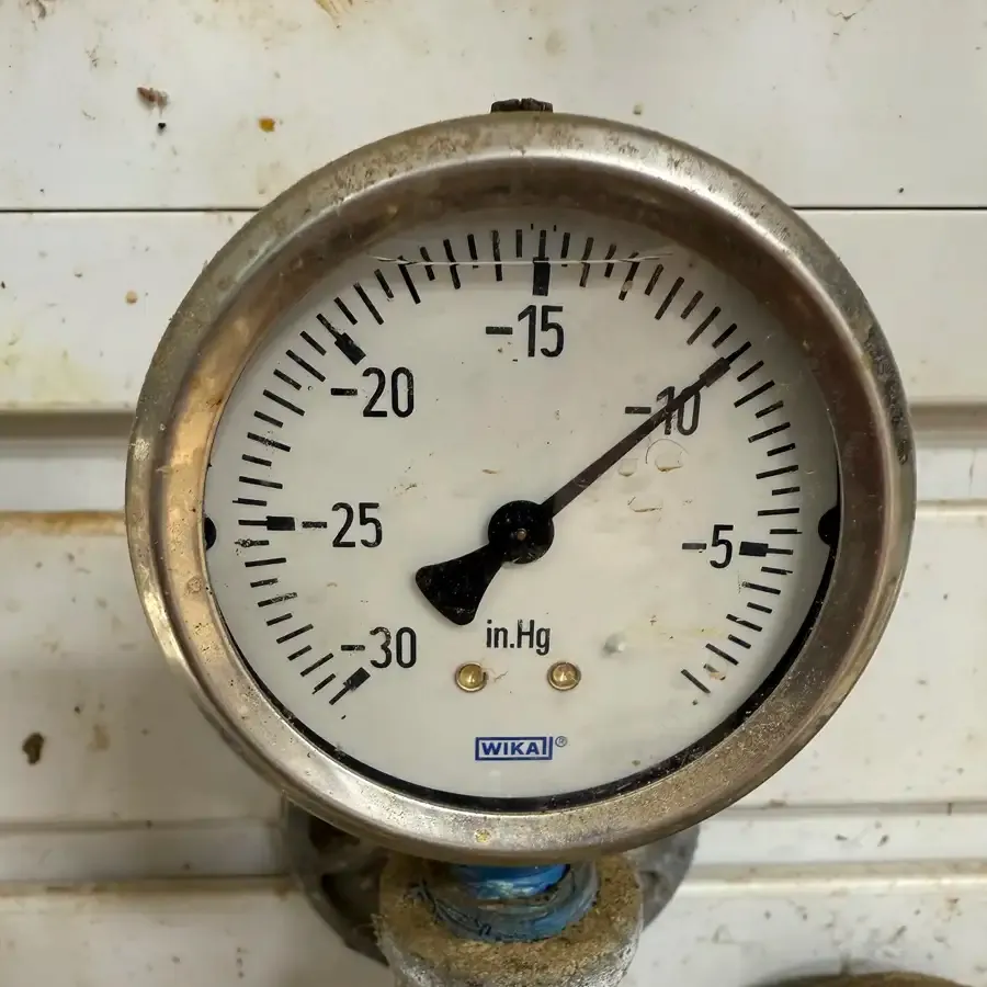 Close-up of vacuum gauge set just under 10 inHg with warning not to exceed this level when milking Dexter cows.
