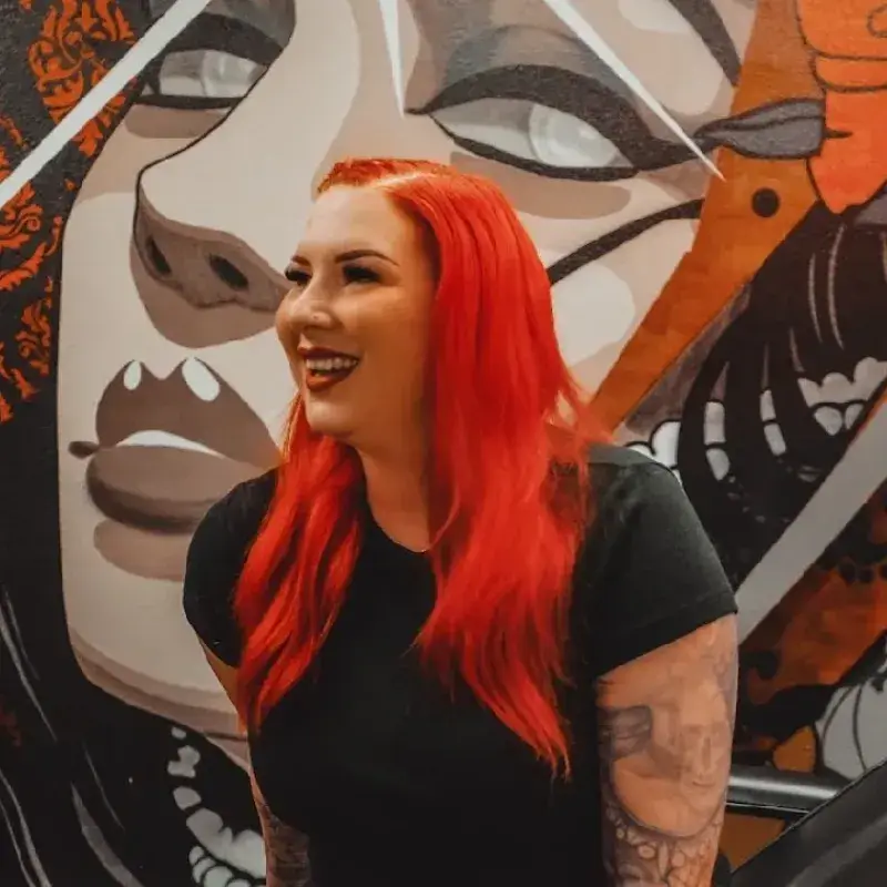 Permanent makeup artist Ms Amber Red stands behind a desk in her studio with the Ms Amber Red sign above her on the wall.
