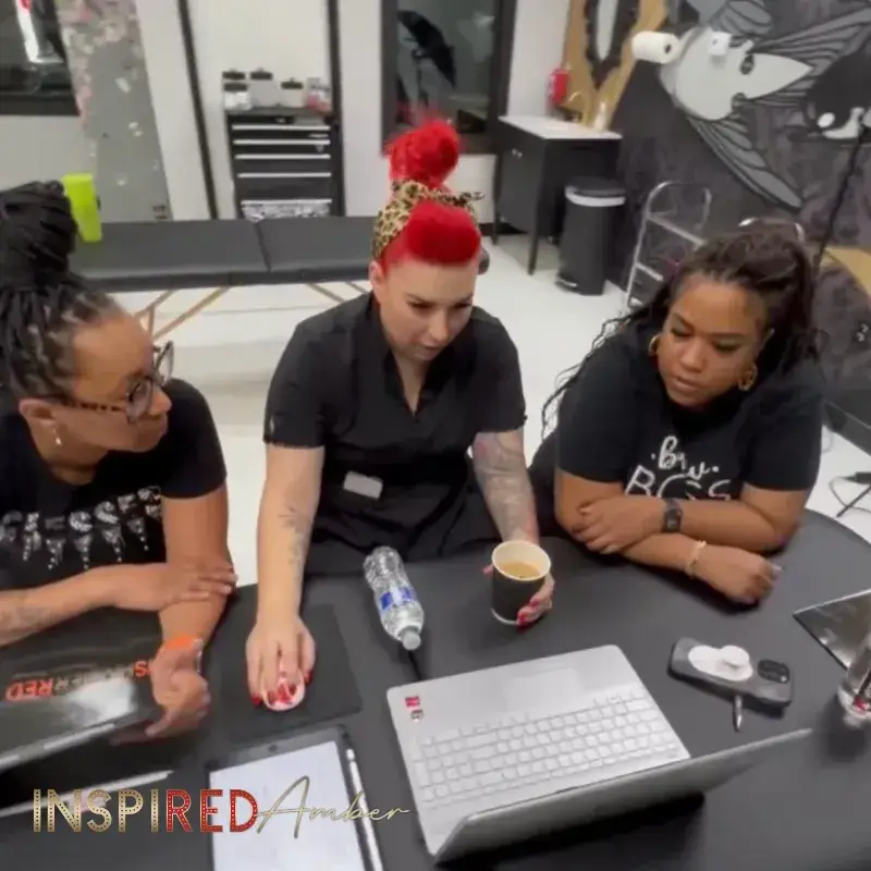 Three women gathered around a laptop during a permanent makeup training session in Ms Amber Reds studio.