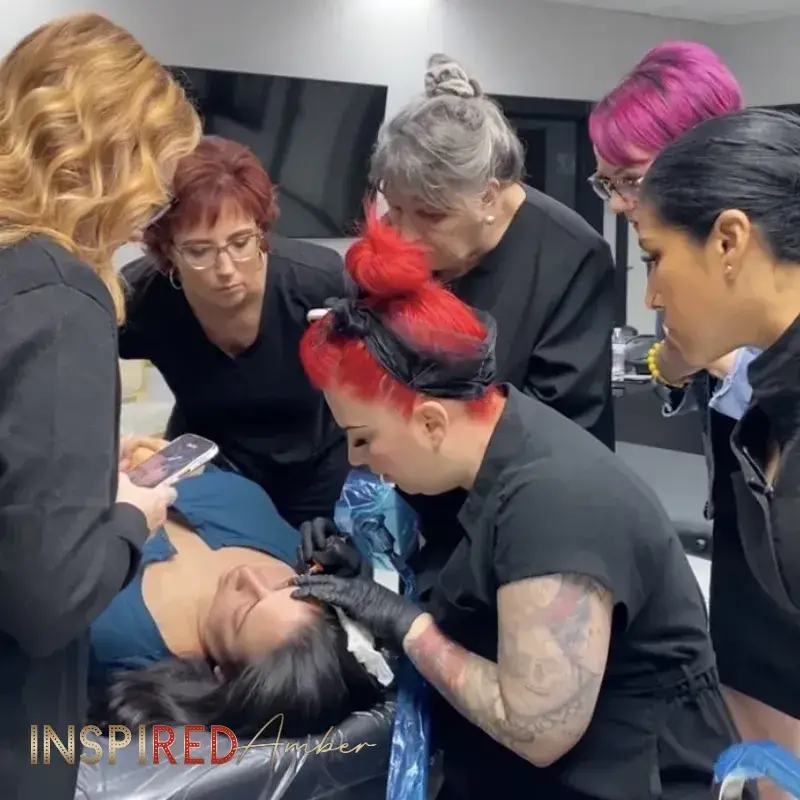 PMU instructor Amber guiding a group of permanent makeup students as they closely watch a live model microblading and shading procedure.