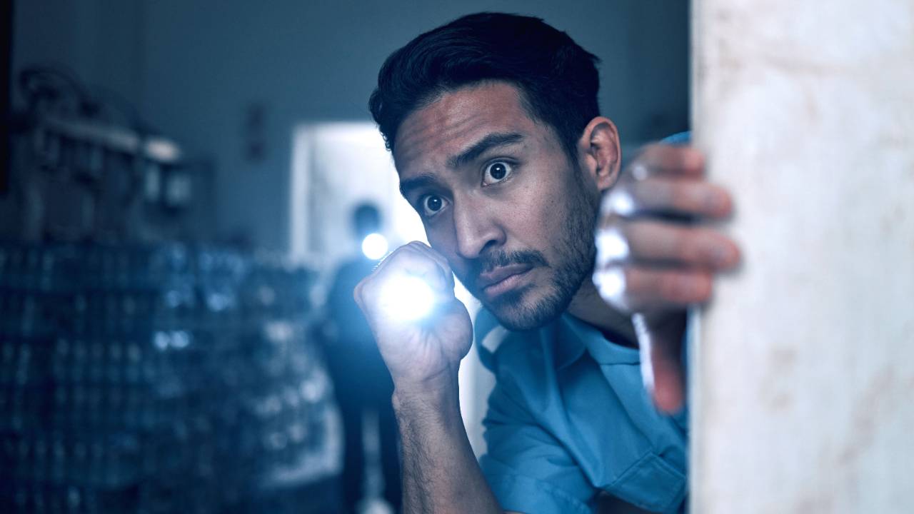 Man peeking hesitantly around a corner with a flashlight