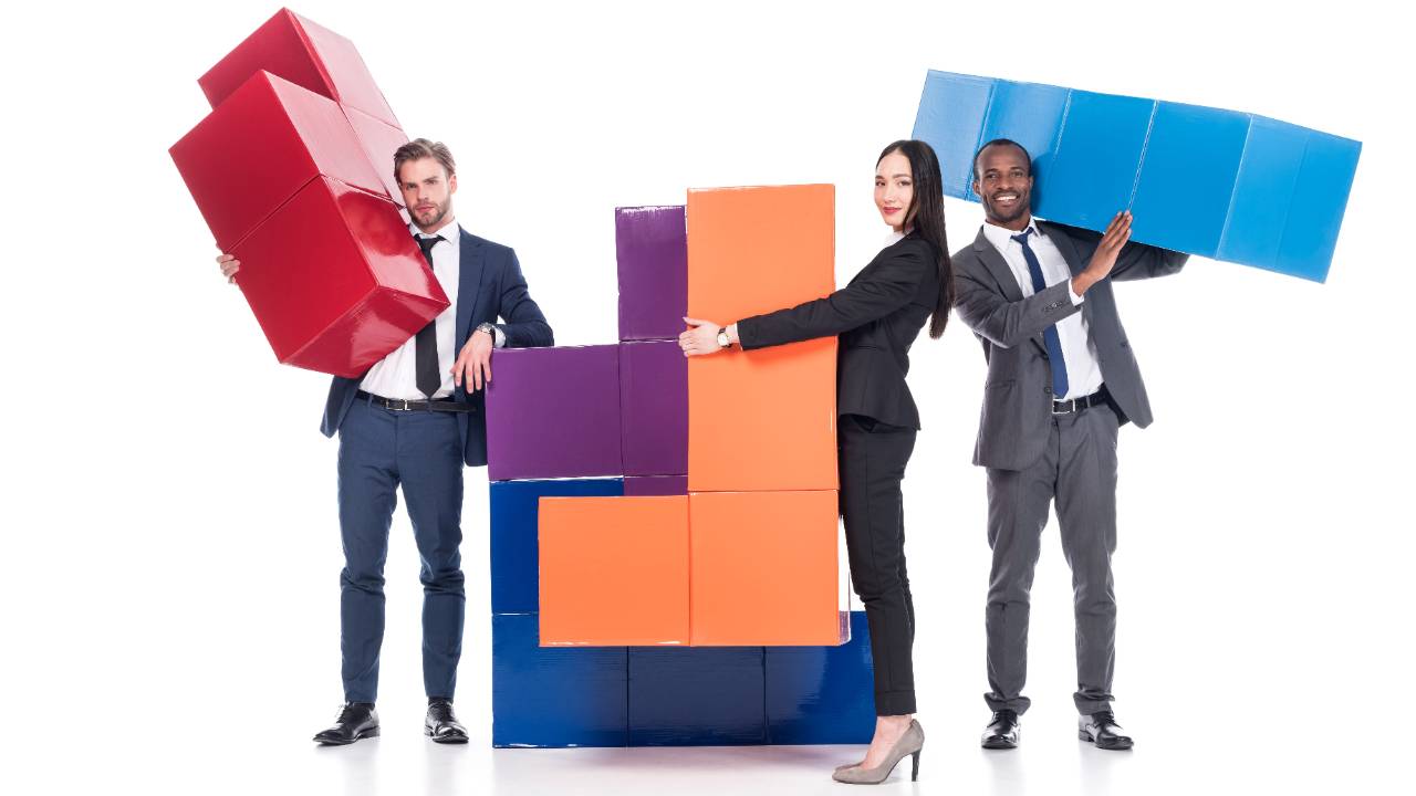 three business people carrying giant Tetris block pieces to fit them together