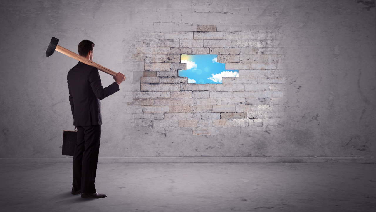 Business man with a sledgehammer looking at sky through small hole in brick wall