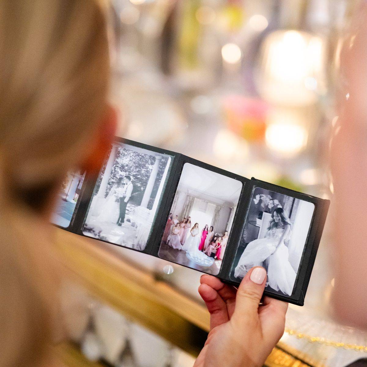 Hands holding a small printed wedding album open to black and white photos at a reception