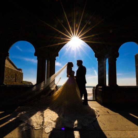 Silhouette of bride and groom under a stone archway with sun flare