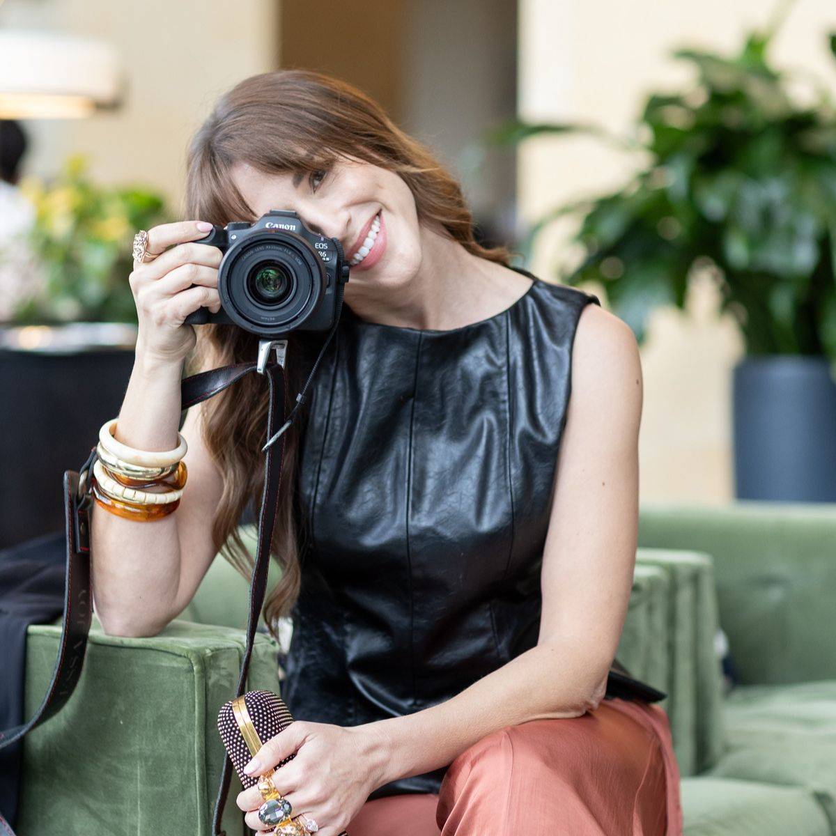Vanessa Joy holding a Canon camera up to her eye, smiling, seated in a lounge chair