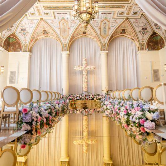 Wedding ceremony aisle lined with pink and white florals in an ornate cathedral-style venue