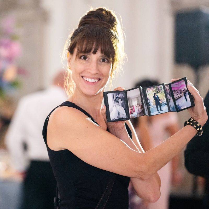 Vanessa Joy at a wedding reception holding up a small same-day album fanned open to show four printed photos