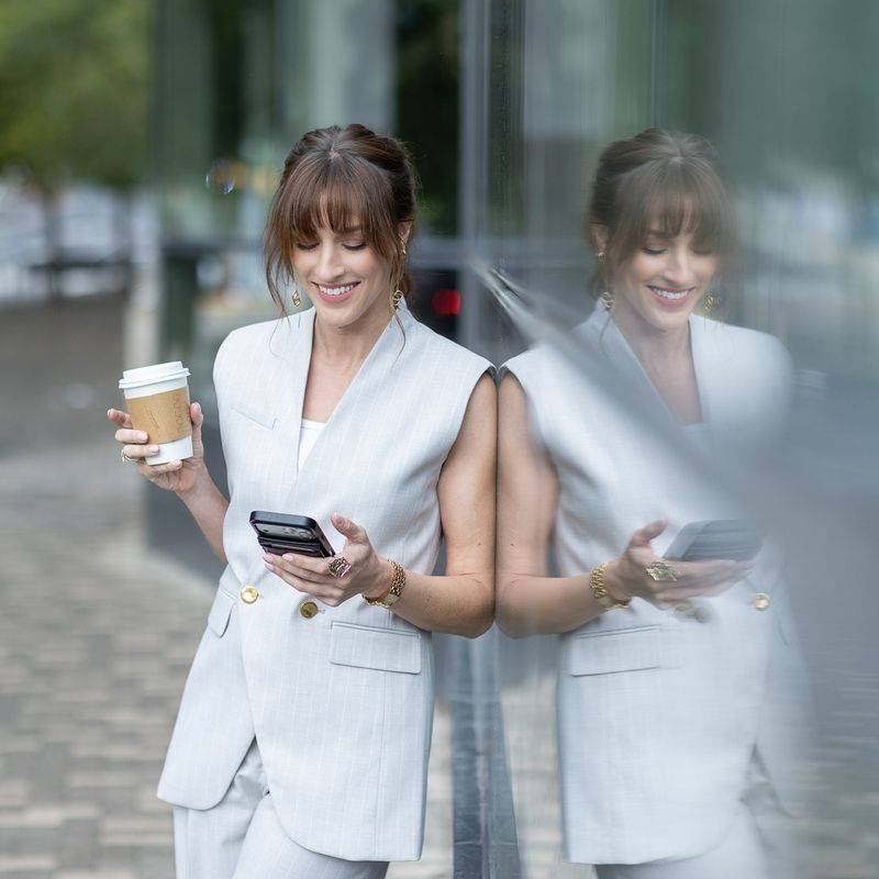 Vanessa Joy walking past a glass building with coffee and phone in hand