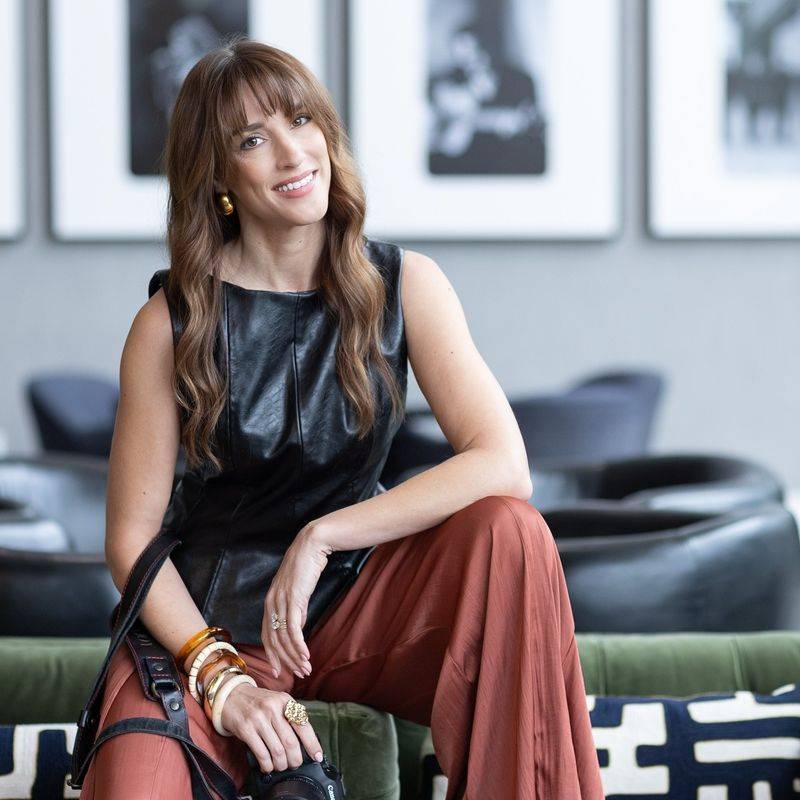 Vanessa Joy sitting with her camera in a lounge with a black-and-white photo gallery wall