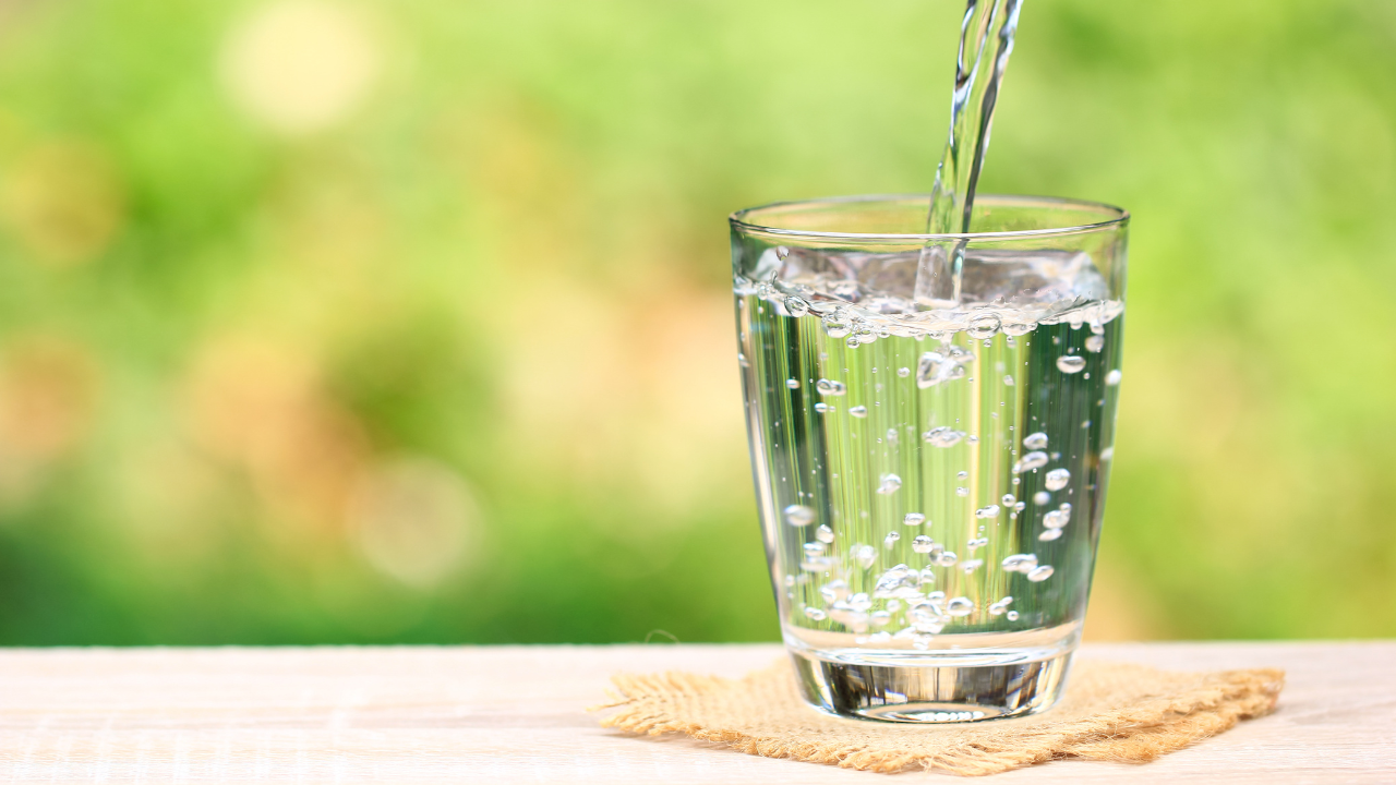 Clear fresh water being poured into a glass against a soft green bokeh background, representing the Inner Empire™ truth that hydration is not a wellness trend but the most foundational support a woman in midlife can give her brain and body.