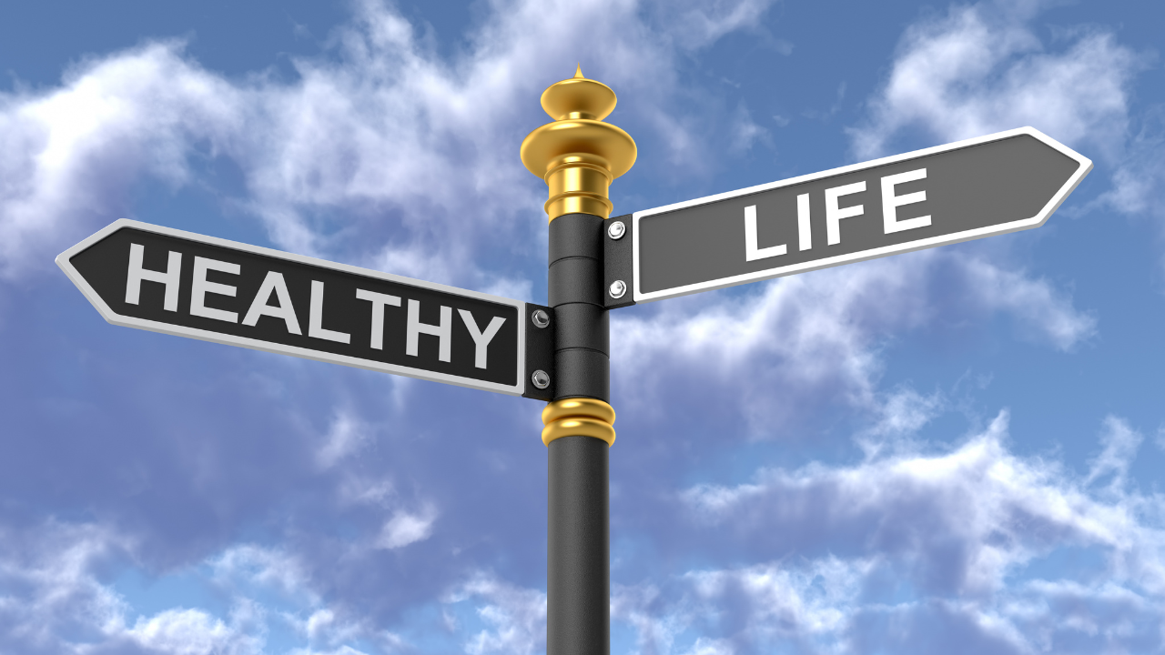 A gold and black directional sign post with arrows pointing to Healthy and Life against a bright blue sky, representing the choice women in midlife face between decline and the Upgrade Phase.