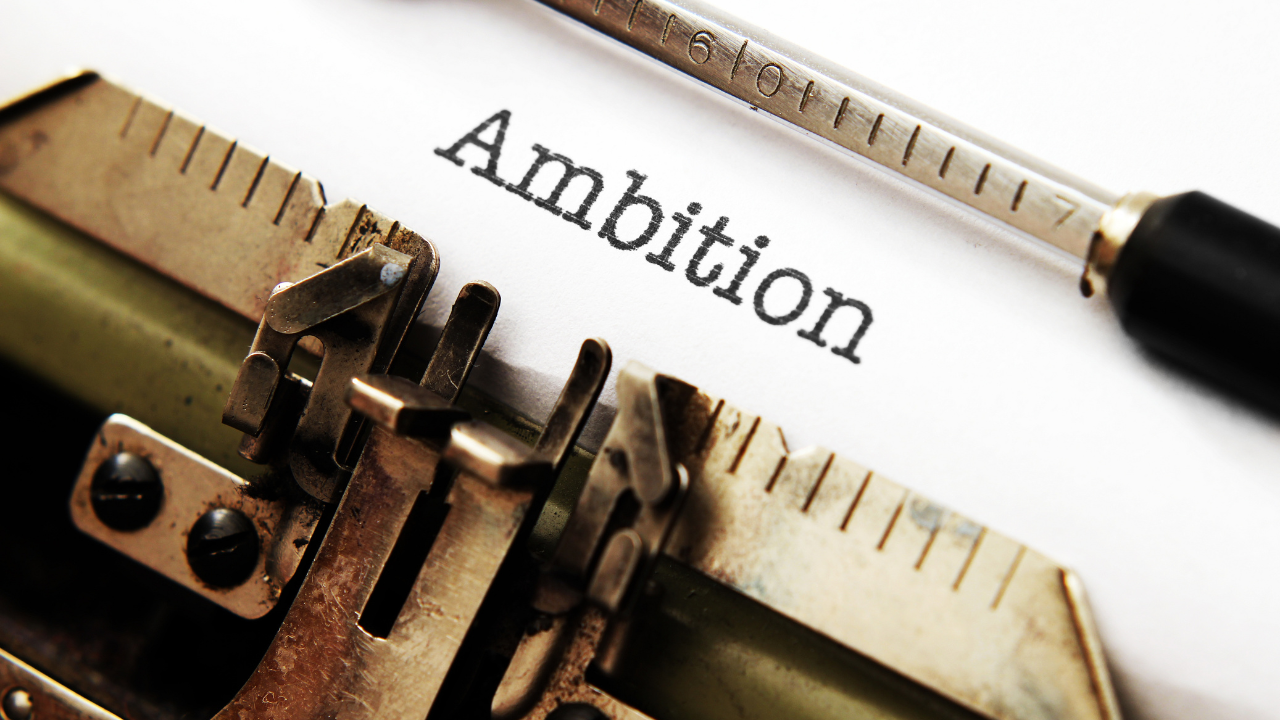 A vintage typewriter with the word Ambition typed on white paper, representing the Inner Empire™ truth that ambition and spiritual grounding are not opposites but two expressions of the same whole woman.