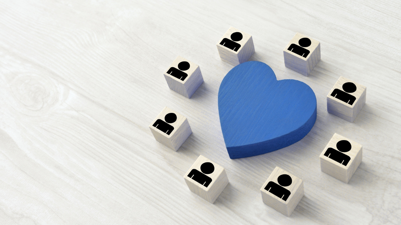 A blue wooden heart surrounded by wooden blocks with person icons, representing how relationships surround and affect wellbeing.