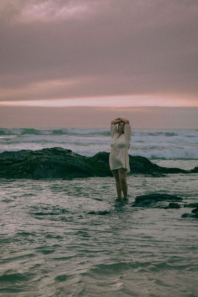 Inês na praia ao entardecer, com o céu rosa