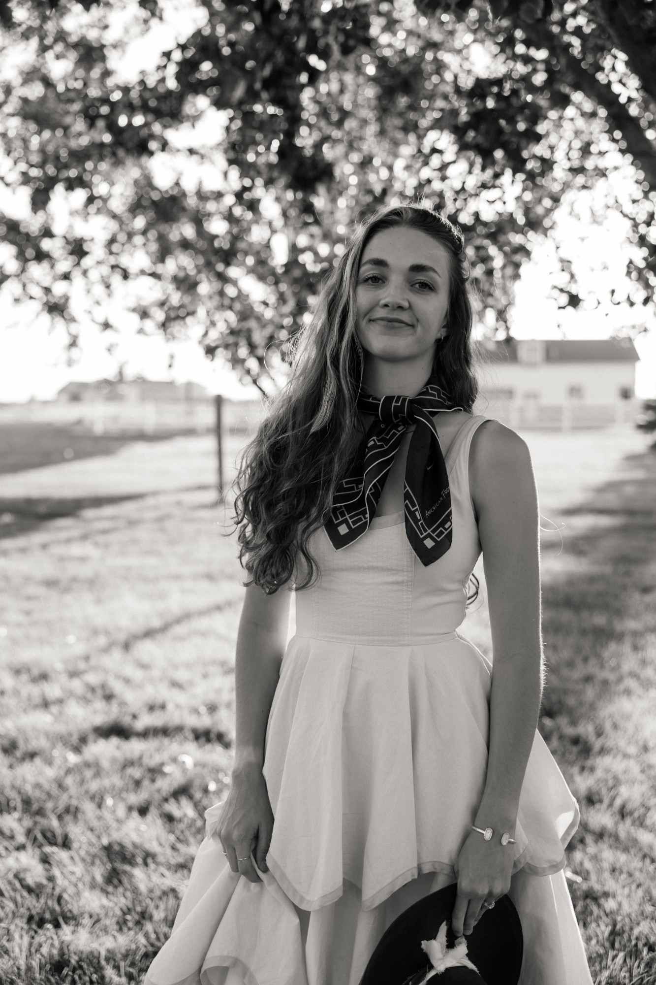 Mya Nichol smiling under a tree in a white dress and scarf