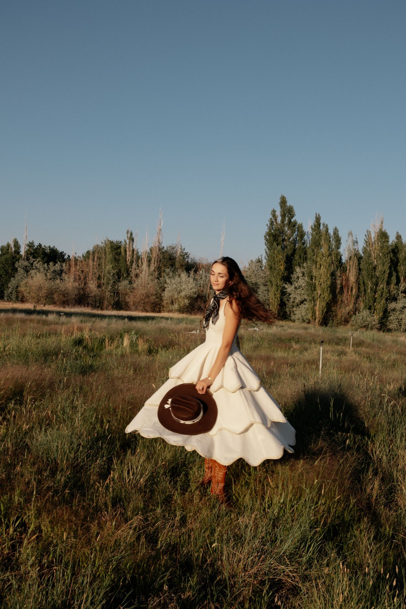 Mya twirling in a white dress in a field, holding a brown hat