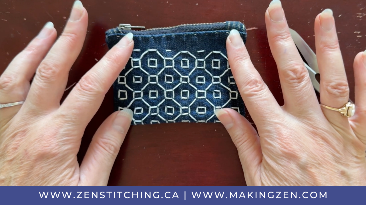 A white woman's hands hold a small coin pouch that has been stitched with the zenigata zashi stitch.