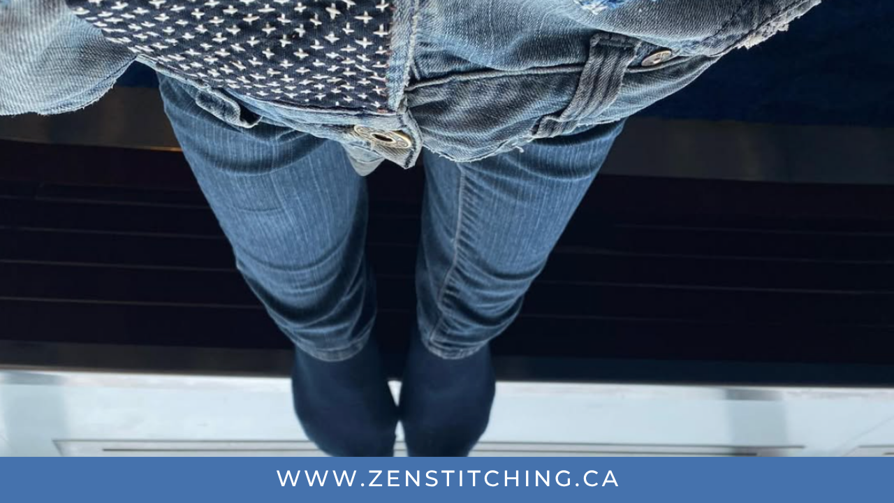 A pair of legs in jeans sticks out from underneath another pair of jeans being mended. The photo appears to be upside-down. The bottom reads www.zenstitching.ca