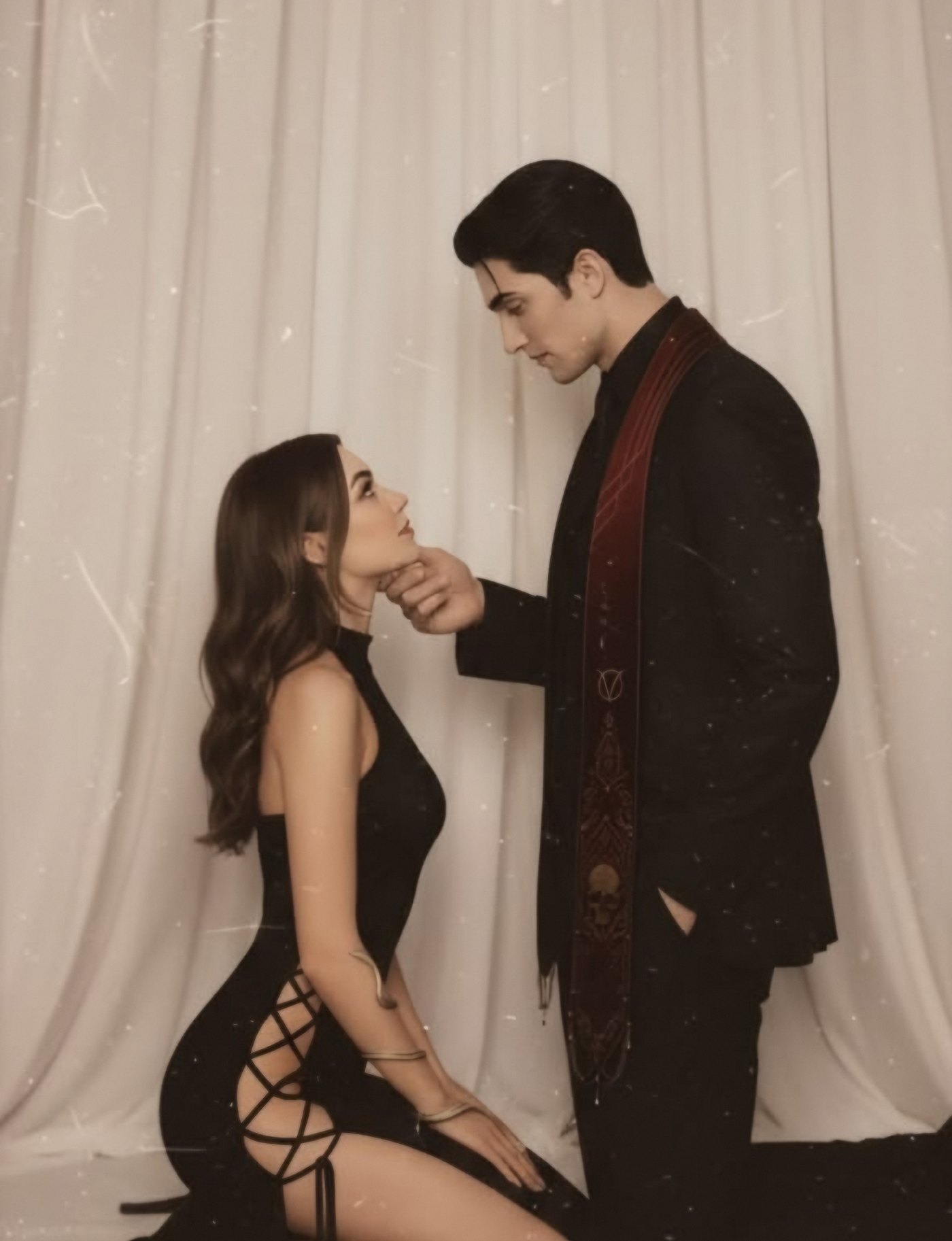 A woman in a black dress kneels before a man in a dark suit as he gently lifts her chin