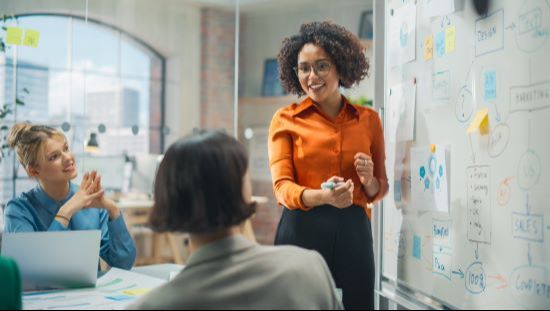 A women standing in front of a whiteboard brainstorming with collogues in a conference room