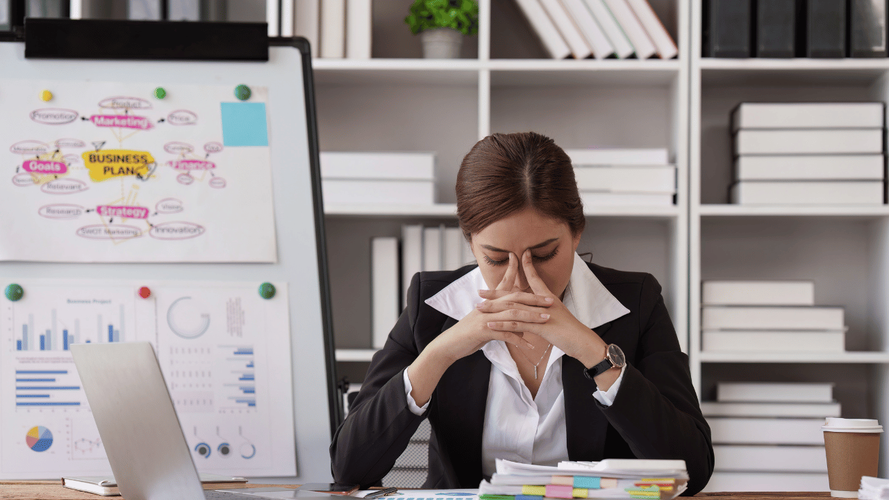 business woman with fingers on temples and flip chart with business plan in background