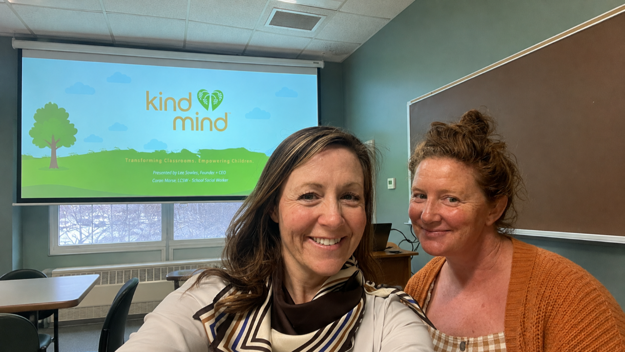 Lee Sowles and Caron Morse smiling in a classroom in front of a Kind Mind presentation slide