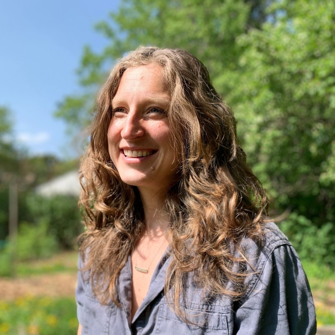 Photo of Erica Marcus, Mindfulness Educator and Collaborative Author. Marcus stands outside in a denim shirt with green trees and grass in the background.