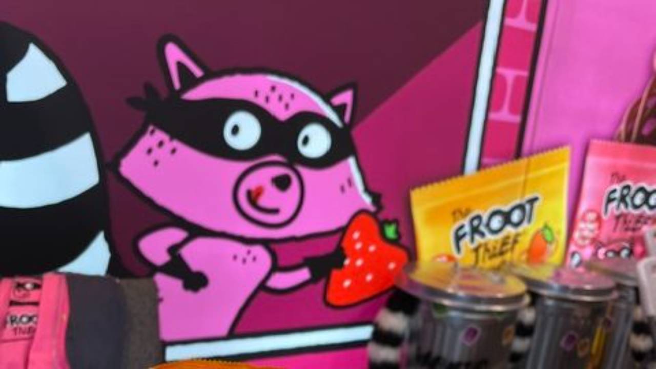 Cartoon racoon mascot from the brand froot thief holding a strawberry.
