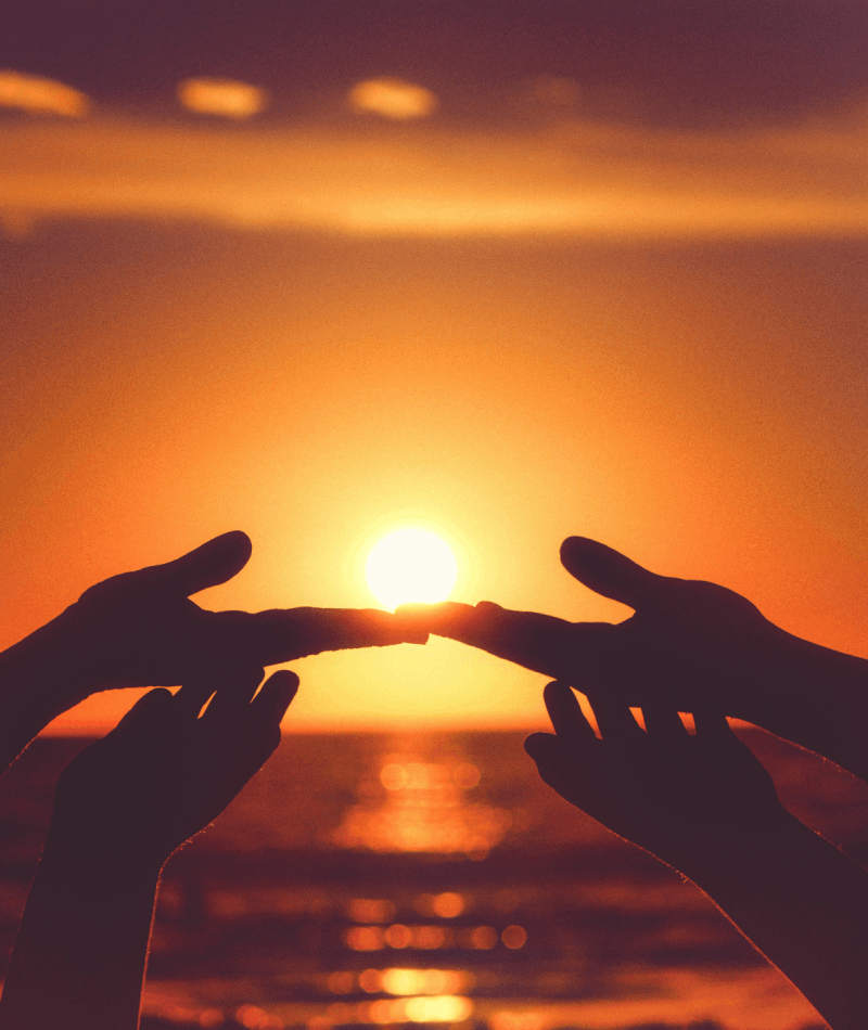 Hands reaching toward sunlight over the ocean