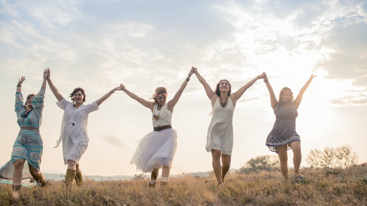 Group of women walking in nature with arms raised holding hands 