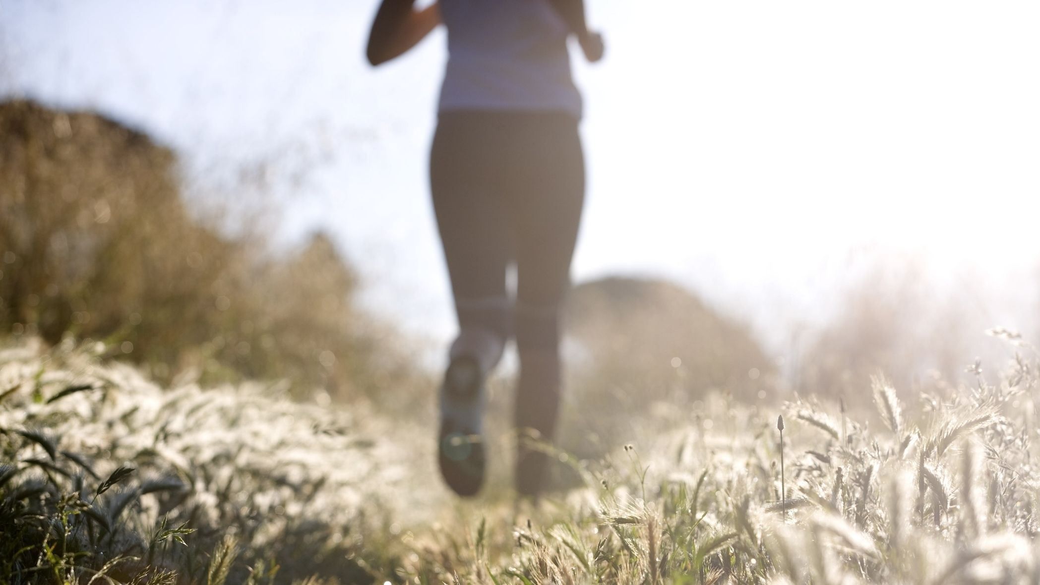 Woman running outdoors on a sunlit trail, representing VO2 max, cardiovascular fitness, healthy aging, and longevity.