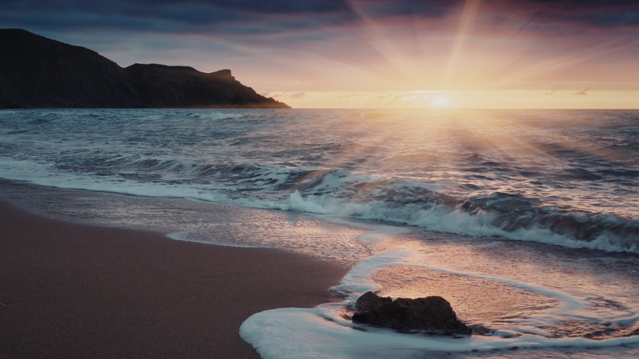 Sunrise over a calm beach with soft light reflecting on the water, symbolising new beginnings and moving forward in life