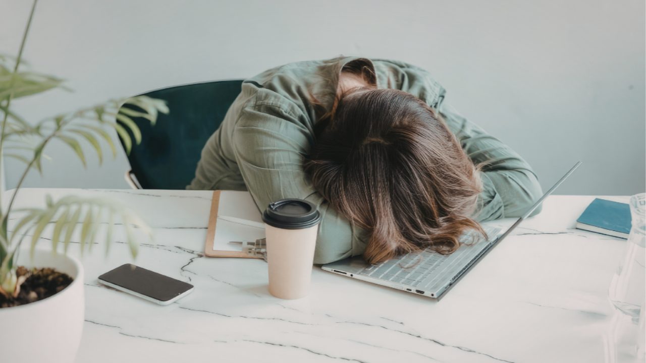 Woman sitting at a desk with head in hands feeling stressed and overwhelmed while working on a laptop
