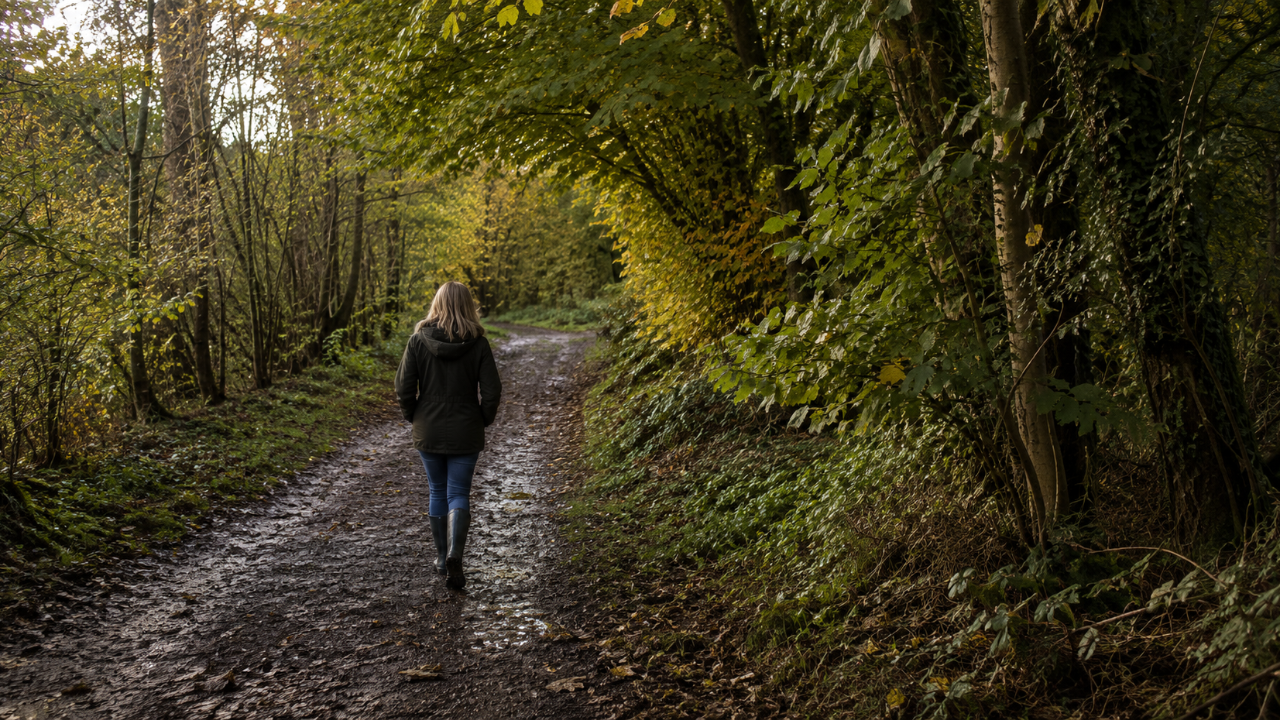 Woman walking away through a peaceful forest, surrounded by tall trees