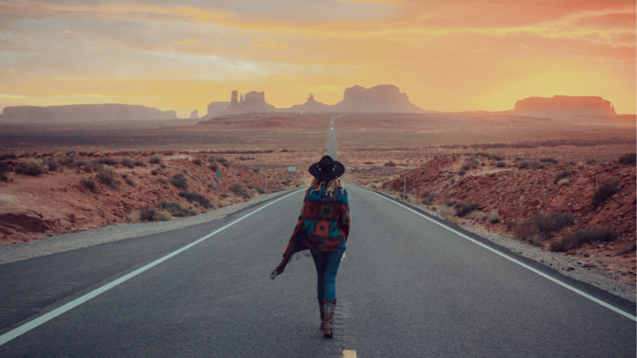 A lone figure walking along a paved road towards a sunrise on an open horizon, symbolising hope, direction, and new beginnings.
