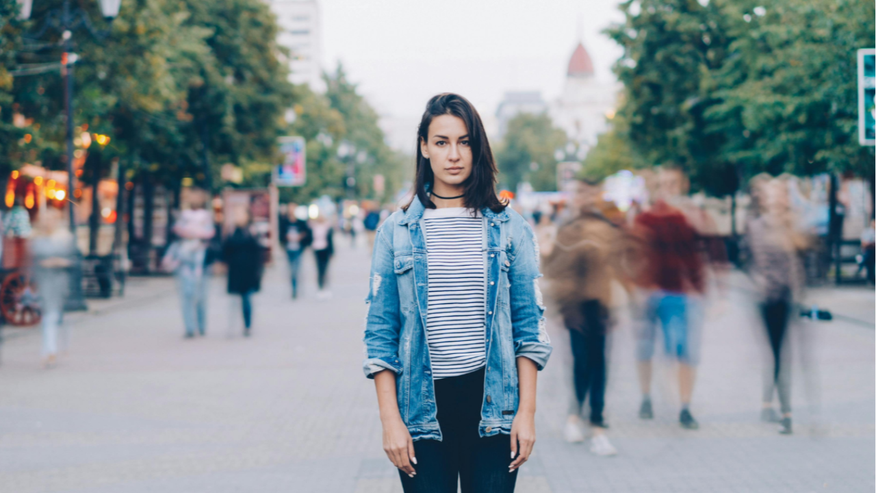 Woman standing alone in busy city street with blurred crowd and motion in background