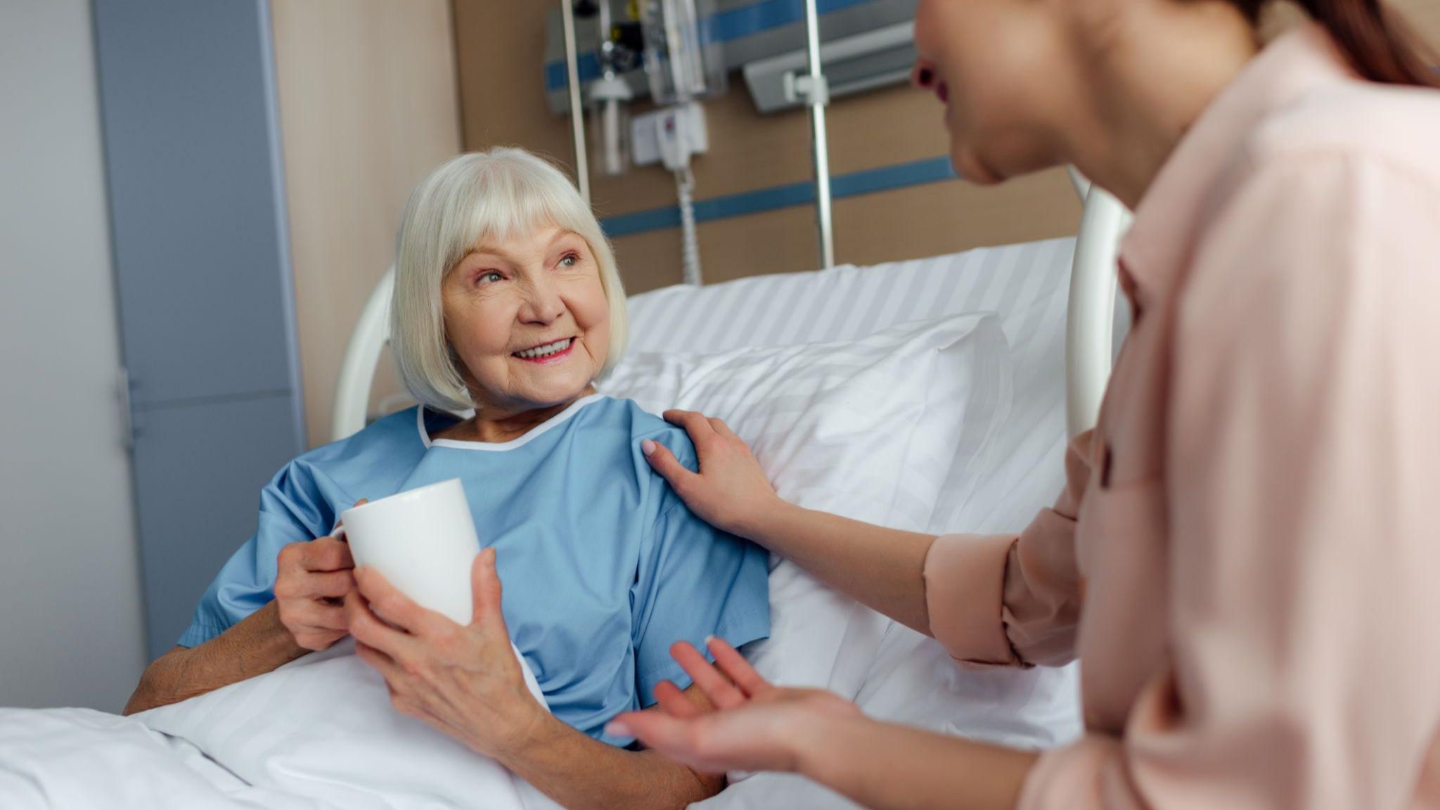 Senior woman in hospital bed sharing tea and a heartfelt conversation with a younger patient, showing kindness and connection