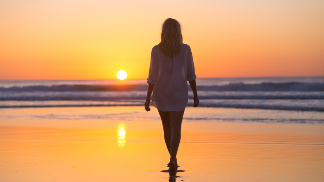 Woman walking on beach at sunset reflecting on life and growth
