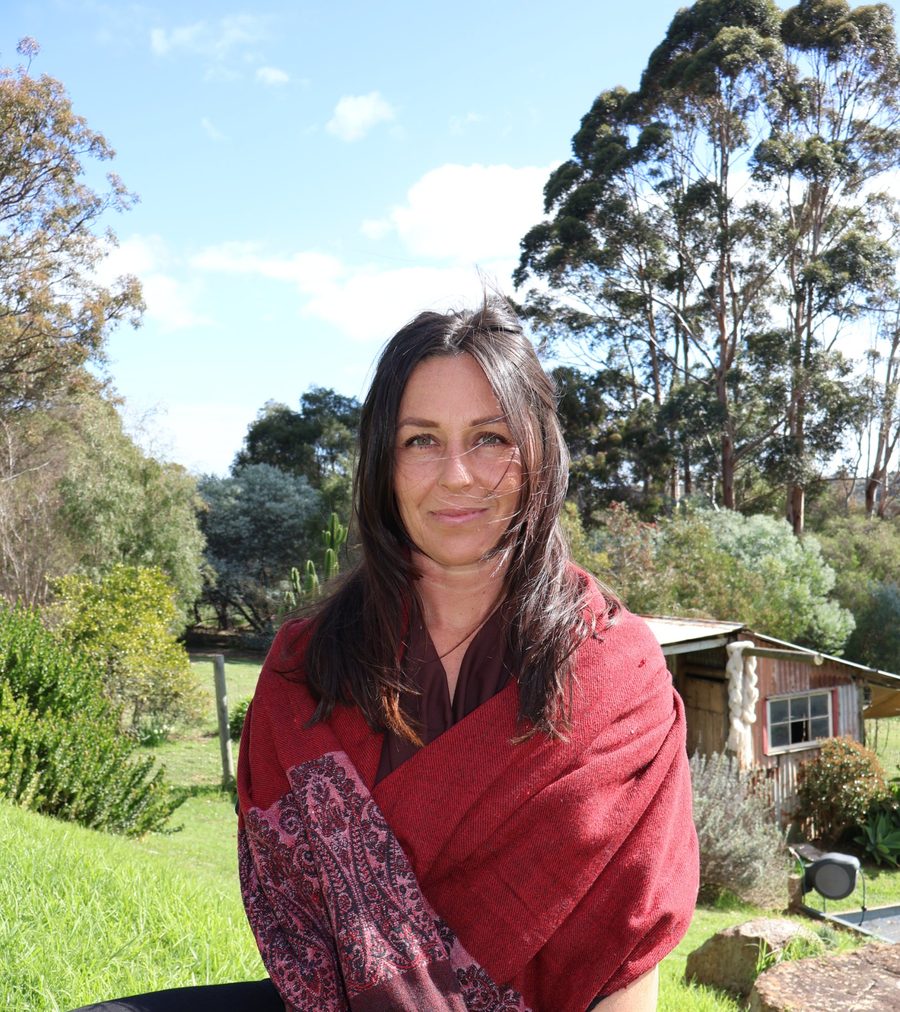 Rhiannon Heins sitting on a rock in her garden, wrapped in a red shawl