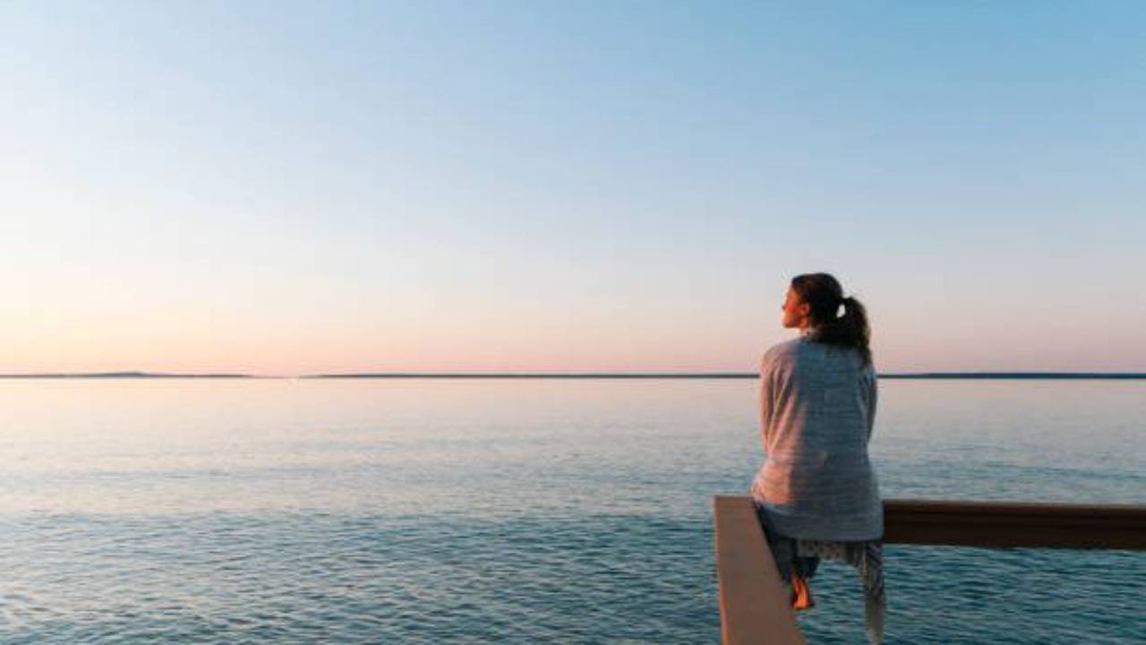 Woman sitting on a dock railing looking left to the sunset