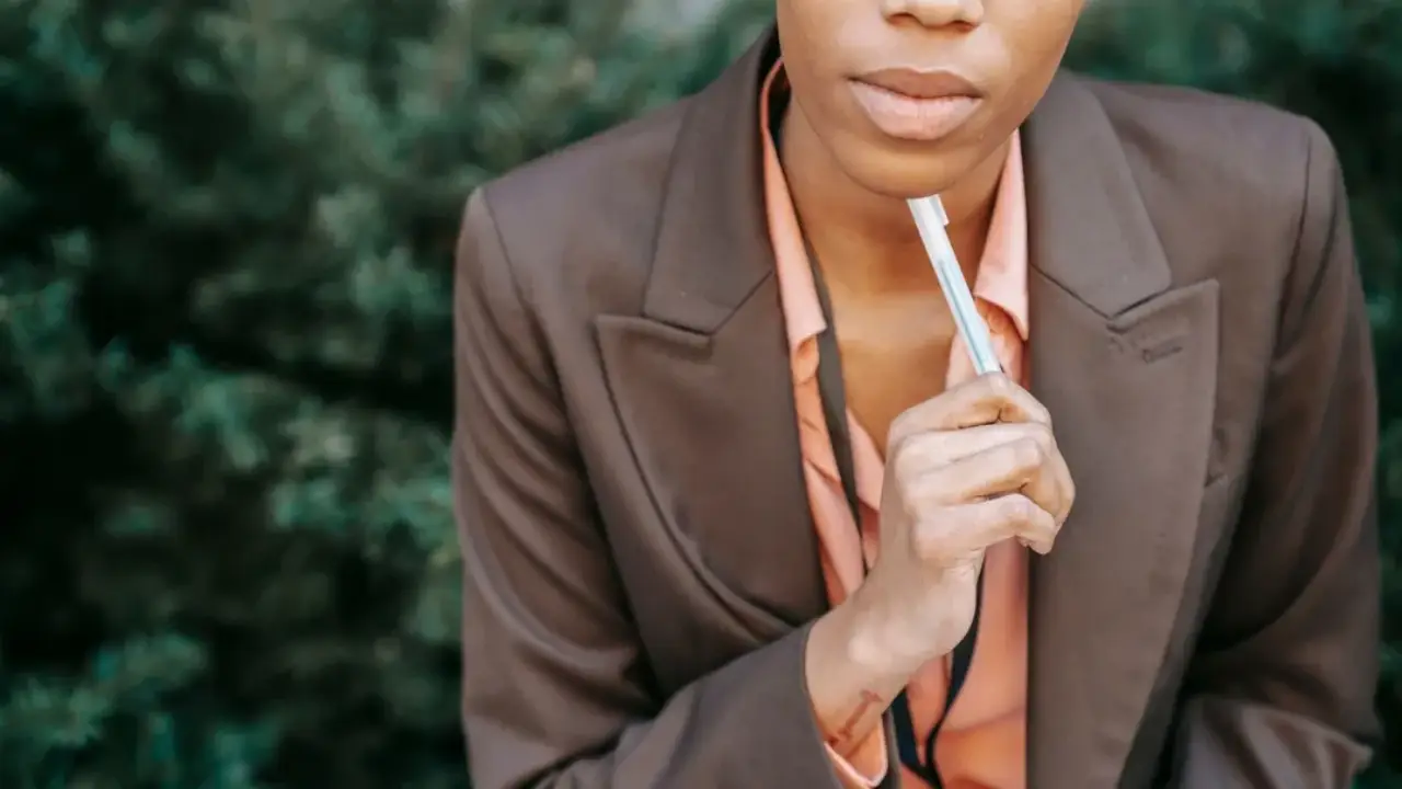 Woman dressed professionally holding pen to chin in thought