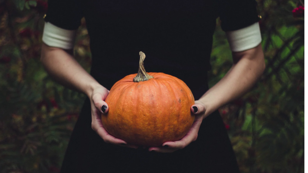 women in black holding an orange pumpkin between her hands